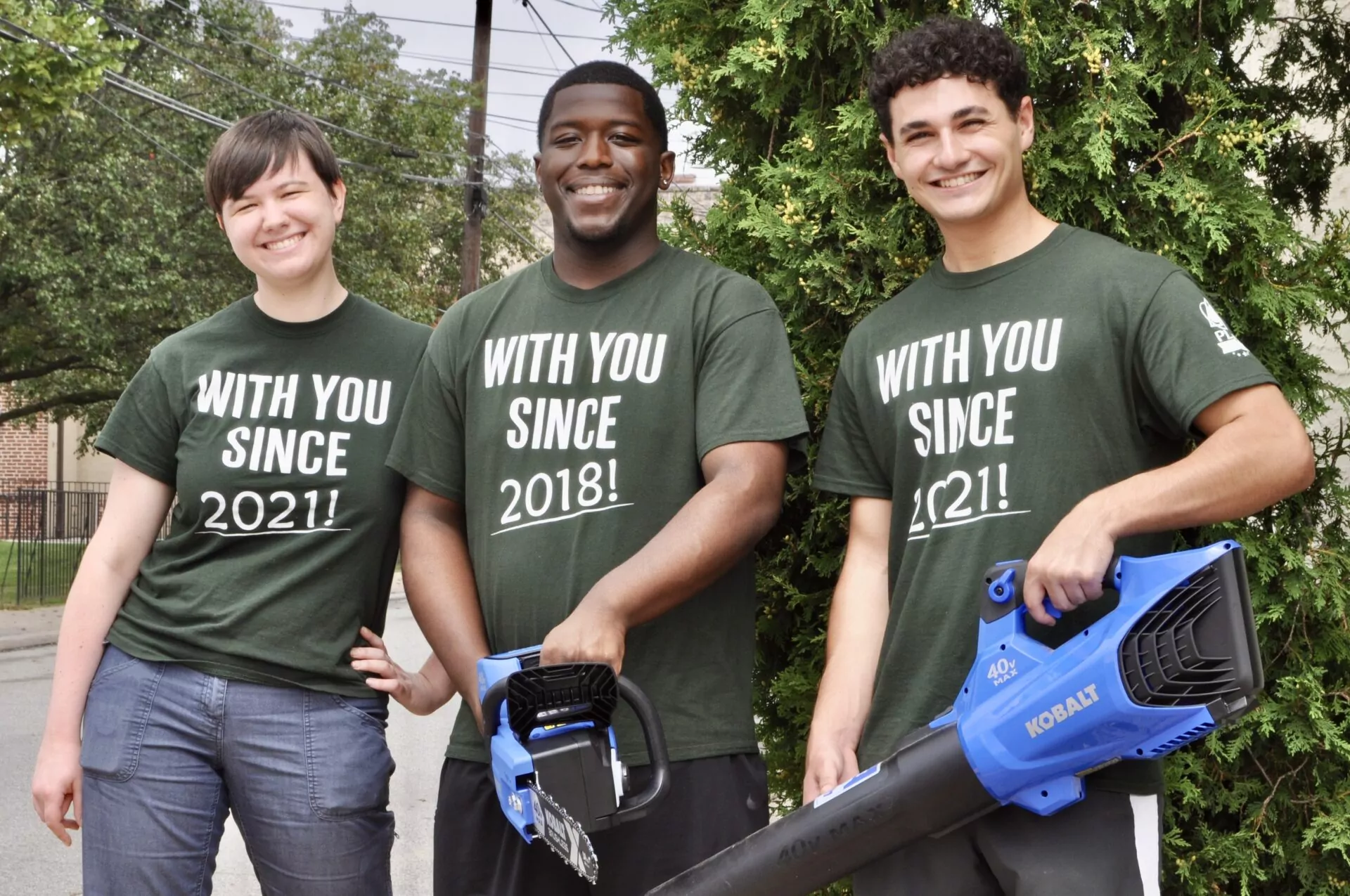 Three volunteers smiling and holding tools